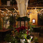 Estatua religiosa iluminada rodeada de plantas en patio.